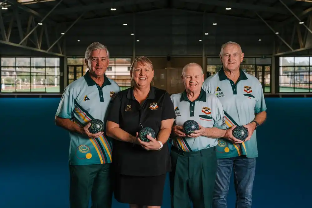 Group of four lawn bowls club members standing indoors holding lawn bowls.